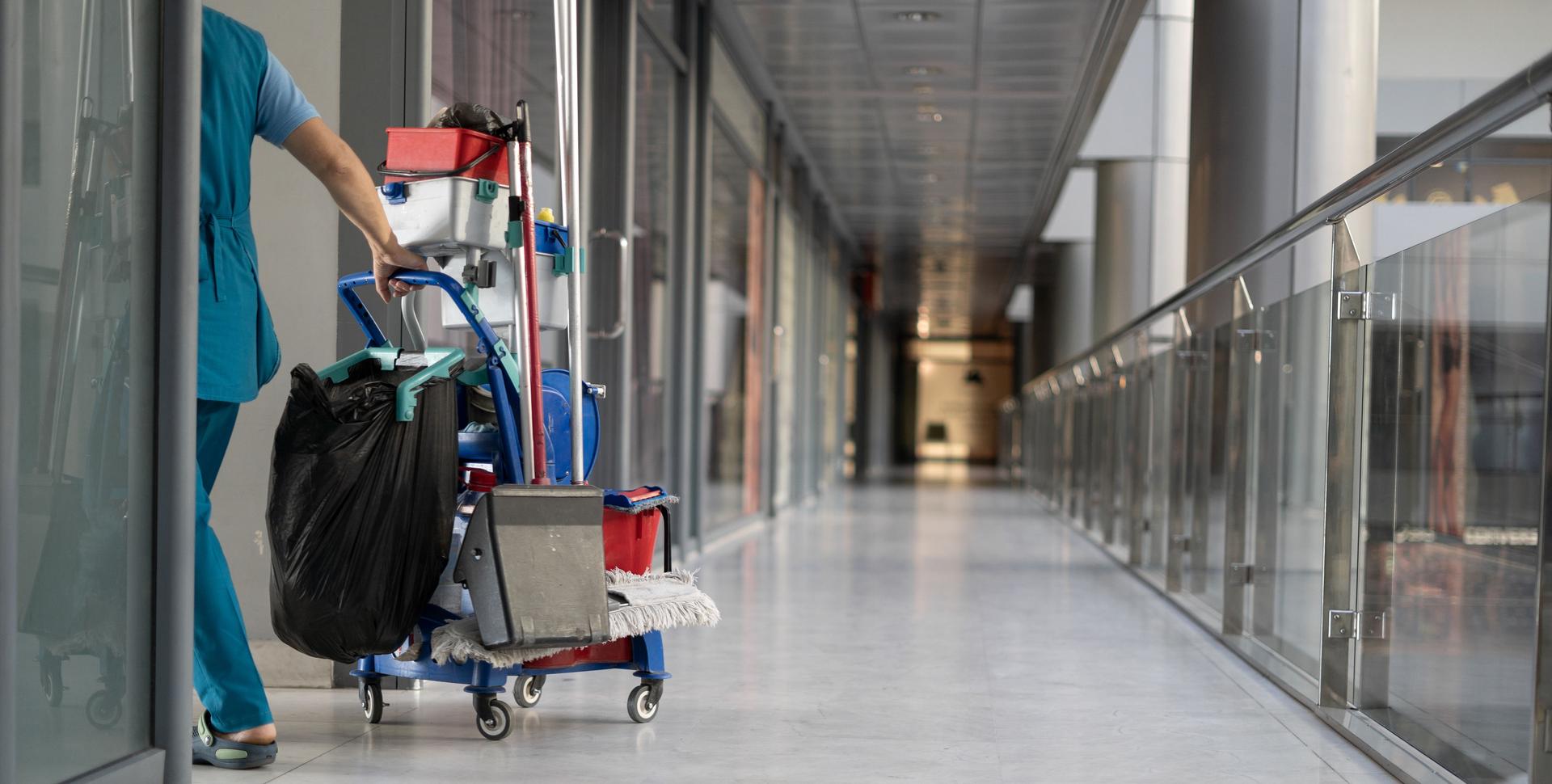 A team of employees pull a trolley for cleaning offices. Woman cleaner is engaged in work.